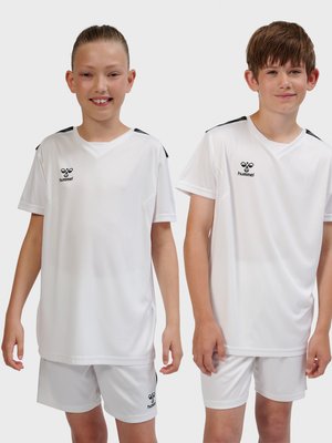 Deux enfants souriants portant des maillots et shorts de sport blancs assortis avec des logos noirs, debout devant un fond uni.