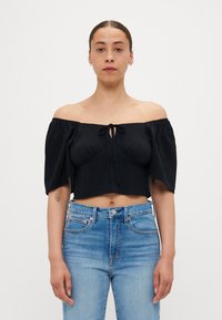 Svart av-shoulder cropped topp med pufferm, samlet halsbånd og glatt stoff. Sammen med lyseblå høyt liv bukser.