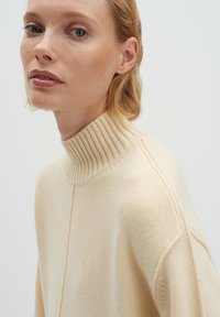 Beiger Rollkragenpullover aus weichem Strickmaterial. Mit geripptem Kragen und Seitennaht, lockerer Passform und strukturierter Stoff.