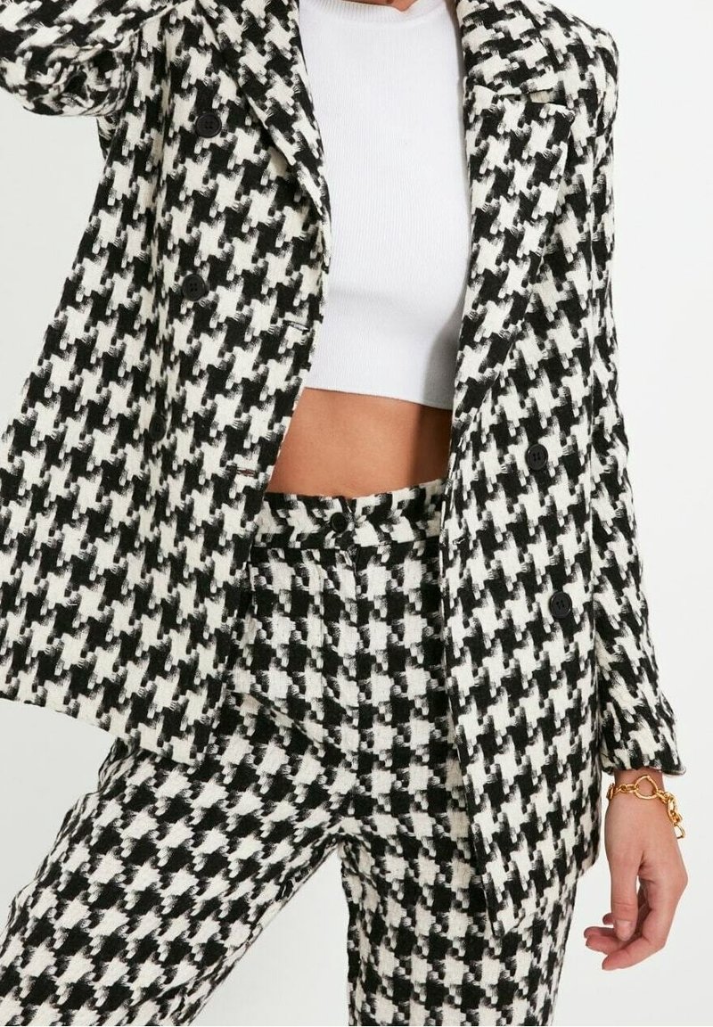 Blazer a fantasia houndstooth bianco e nero con pantaloni abbinati. Tessuto strutturato, design doppiopetto e dettagli con bottoni.
