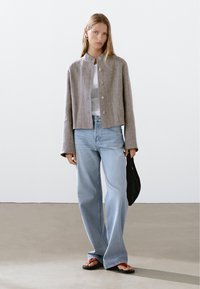 Gray linen cropped jacket with round neckline and button front, paired with light blue high-waisted jeans and black tote bag. Flip-flops worn.