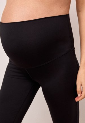 Schwangere Person trägt schwarze Umstandsleggings mit hohem, elastischem Bund, der den Bauch stützt.