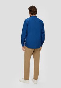 Blauwe langekiel met knopmanchetten, rugpand en een afgeronde zoom. Gecombineerd met beige chinos en witte sneakers.