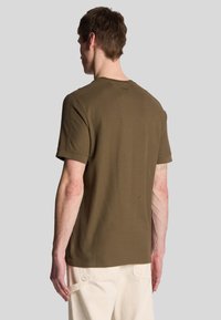 T-shirt verde oliva a maniche corte in un morbido mix di cotone, con scollo rotondo e vestibilità rilassata, con dettagli di cucitura sulle maniche.