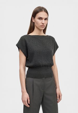 Un mannequin aux longs cheveux bruns porte un haut en maille gris anthracite à manches courtes et un pantalon assorti, sur un fond uni clair.