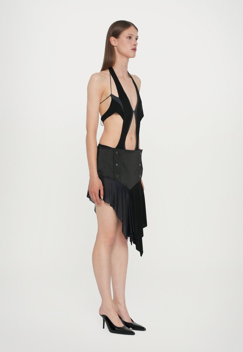 Black asymmetric dress with cutouts and a halter neck, featuring a textured bodice and a ruffled hem, paired with black high heels.