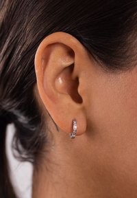 Silberne Creolen mit polierter Oberfläche und kleinen eingebetteten Kristallen, seitlich gezeigt, getragen am menschlichen Ohr.