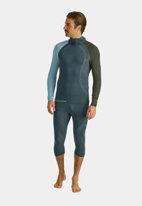 Long-sleeve, two-tone base layer shirt in dark blue and green with a high collar, paired with matching fitted pants, made from stretchy fabric.