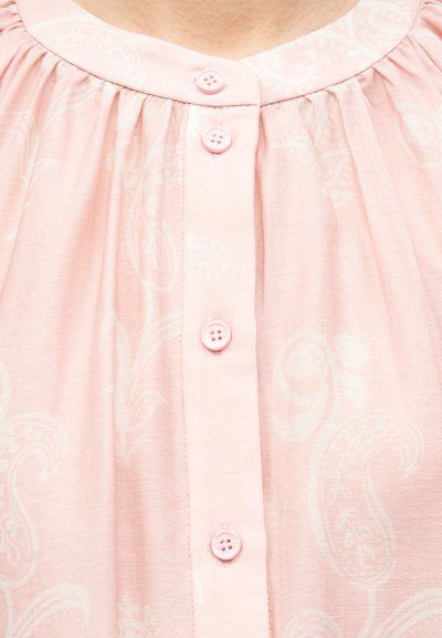 Κοντινό πλάνο ενός ανοιχτόροζ μπλουζιού με διακριτικά σχέδια πεϊсли και τέσσερα ταιριαστά ροζ κουμπιά κατά μήκος της εμπρόσθιας λωρίδας.