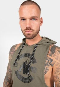Olivgrüner �ärmelloser Hoodie mit einem schwarzen Grafikdruck, der einen Gorilla, Text und eine amerikanische Flagge zeigt. Mit Zugband in Schwarz und Weiß.
