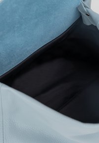Lyst blå lædertaske med en blød suedeflap. Indvendig er der sort stof, der har en glat tekstur og en lynlås lomme til opbevaring.