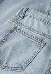 Tela de mezclilla azul clara con un bolsillo trasero cosido y presilla para el cinturón, mostrando textura detallada y costuras con hilo naranja.