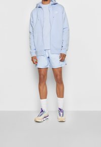 Ljusblå zip-up hoodie, matchande t-shirt och shorts. Vita strumpor, beige sneakers med lila och turkosa accenter. Enkelt, avslappnat design.