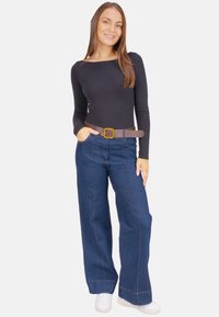 Pantalon en jean à jambes larges de couleur bleu foncé, avec une ceinture en cuir marron à boucle carrée, associé à un haut à manches longues noir et des baskets blanches.