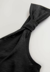 Sorte stof med en blød tekstur; har et snoet knudedesign øverst, hvilket skaber en unik form. Minimalistisk og diskret.