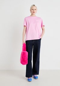 Camiseta de algodón rosa claro con mangas cortas, combinada con jeans de denim oscuro de pierna ancha. Sosteniendo un bolso de piel sintética rosa brillante y usando zapatillas deportivas azules.