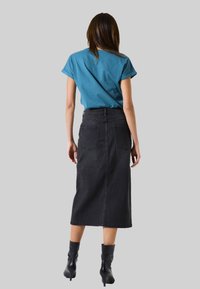 Chemise turquoise à manches courtes assortie à une jupe en denim noire taille haute, arrivant aux chevilles. Le mannequin porte des bottes à talons noires. Design et coupe simples.