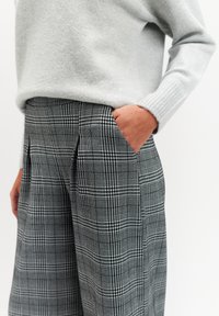 Czarne i białe spodnie w kratę z teksturowanego materiału, z bocznymi kieszeniami i zakładkami. Noszone z jasnoszarym swetrem.