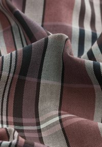 Textil con un patrón de cuadros que presenta tonos de burdeos, negro y blanco. La tela está tejida con una textura suave y líneas de rejilla visibles.