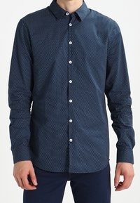 Navy blue long-sleeve shirt with white geometric pattern, button-down collar, and front button closure. Smooth fabric with fitted design.