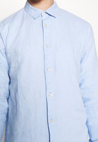 Himmelblaues Leinenhemd mit klassischem Kragen, das eine glatte Textur aufweist und über fünf Knöpfe auf der Vorderseite verfügt.