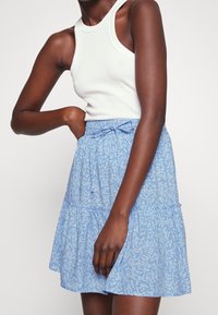 Gonna a strati con motivo floreale blu chiaro, dotata di cintura elastica e stringa. Tessuto liscio con una leggera consistenza fluida.