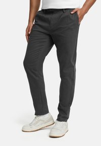 Sivé prispôsobené nohavice s plochým predným dielom, šikmými bočnými vreckami a hladkou, ľahkou tkaninou. Kombinované s bielymi teniskami.