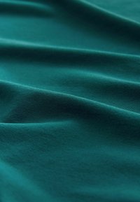 Nahaufnahme von türkisfarbenem Stoff mit sanften Falten und subtiler Textur, die feine Strickdetails und eine glatte Oberfläche hervorhebt.