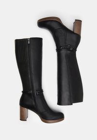 Bottes noires en cuir jusqu'au genou avec une finition texturée, un talon épais, des fermetures à glissière sur les côtés et un détail de sangle ajustable.