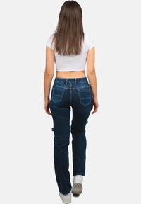 Jeans blu scuro con vestibilità slim e vita media. Presentano due tasche posteriori e sottili dettagli di cucitura. Stile abbinato a un crop top bianco.