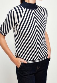 Pletený svetr s krátkým rukávem, vysokým límcem a diagonálním pruhovaným vzorem v námořnické modré a krémové barvě, s žebrovaným lemem a manžetami a mírnou texturou.