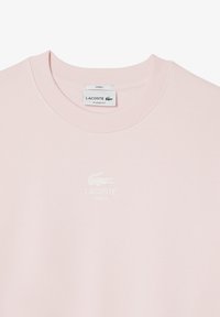 Felpa rosa chiaro in cotone. Presenta un colletto a costine e un logo Lacoste bianco con un emblema di coccodrillo ricamato.