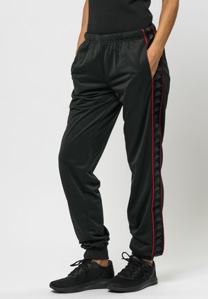 Svarte joggebukser med en blank tekstur, featuring en rød sidelinje og et svart logobånd. Elastisk liv og sidelommer.