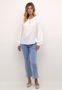 Vit blus med lång ärm, strukturerade ränder och nyckelhålsklippning, i kombination med ljusblå denim, jeans med korta ben och silverfärgade platta skor.