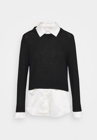 Maglione corto nero a maniche lunghe indossato sopra una camicia bianca con colletto e polsini visibili, presentato su uno sfondo semplice.
