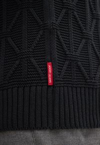 Schwarzer Strickpullover mit einem strukturierten Rautenmuster, einem gerippten Saum und einem roten Etikett mit dem Schriftzug "JOOP! JEANS" auf der linken Seite.