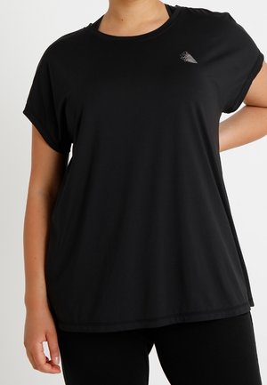 Sort, løstsiddende kortærmet sportst-shirt båret af en person med hånden på hoften mod en ensfarvet baggrund.