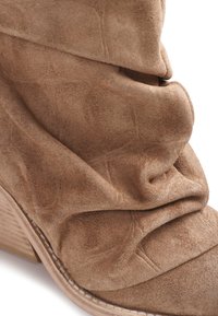 Botte marron en daim décontractée avec talon en bois empilé et couture visible le long du bord de la semelle.