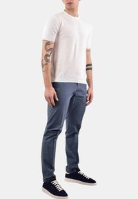 Maglietta bianca a maniche corte in maglia abbinata a pantaloni blu slim-fit e sneaker nere con suola bianca. I pantaloni hanno una texture liscia.