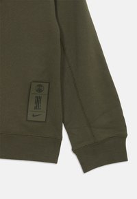 Manga de sudadera verde oscura con un parche de logo bordado que presenta el emblema del Paris Saint-Germain y el swoosh de Nike cerca del puño.