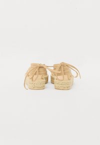 Scarpe espadrillas beige con suola in juta tessurizzata, design con lacci e tomaia in tessuto morbido. La vista posteriore mette in risalto i leggeri lacci e la forma.