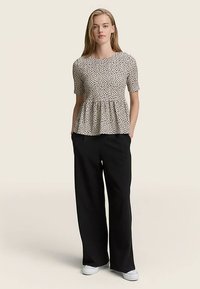 Haut peplum crème à pois noirs, manches courtes, col rond. Associé à un pantalon large noir et des baskets blanches.