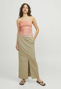Camiseta de melocotón transparente con tirantes finos combinada con una larga falda beige con una abertura frontal; la modelo lleva chancletas negras.