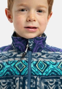 Veste en polaire avec un col haut, présentant un motif géométrique dans des tons de bleu et de violet, contrasté par un design bleu-vert et gris.