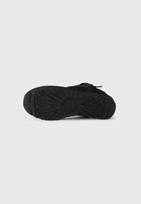 Suola di sneaker nera con gomma testurizzata, caratterizzata da un motivo geometrico e una punta arrotondata, progettata per grip e durata.