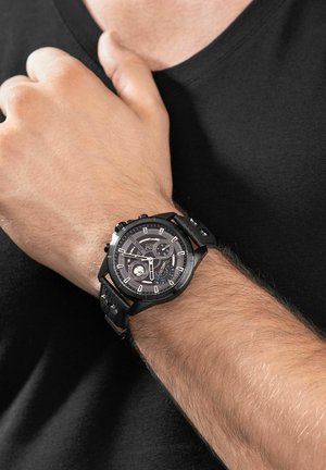 Schwarze Chronograph-Uhr mit strukturiertem Lederarmband, runder Gehäuseform und kontrastierenden weißen Stundenmarkierungen auf einem dunklen Zifferblatt.