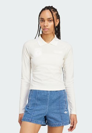 Langärmliges weißes Polohemd mit Kragen, versehen mit einem gestickten Logo, kombiniert mit blauen Denim-Shorts, die einen lässigen sportlichen Stil zeigen.