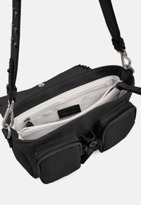 Sac bandoulière en cuir noir avec une fermeture éclair sur le dessus, une doublure intérieure blanche, deux poches externes et une sangle réglable pour plus de polyvalence.