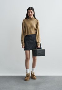 Brūna turtlenecka džemperis, tumši džinsa svārki, balti zeķes, brūni zābaki ar pūkainu apdari, turēt melnu rakstainu rokassomu ar dzeltenu akcentu.