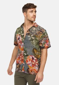 Camisa de botones de manga corta con un diseño de múltiples patrones en tonos tierra, motivos florales y formas geométricas. Tejido ligero.